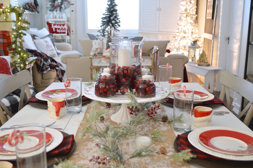 Merry Little Christmas, Fox Hollow Cottage Holiday. Red & Black Buffalo Check Table Setting. Vintage drop leaf dining table & farmhouse metal chairs. Centerpiece of fresh cranberries, mason jars and hurricane/candle on vintage milk glass. 